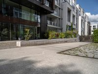 a concrete plaza near apartment buildings with many plants growing in the area behind it,