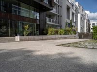 a concrete plaza near apartment buildings with many plants growing in the area behind it,