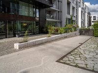 a concrete plaza near apartment buildings with many plants growing in the area behind it,