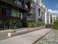 a concrete plaza near apartment buildings with many plants growing in the area behind it,