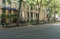 a city sidewalk lined with apartment buildings next to each other, in a row with trees