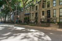 a city sidewalk lined with apartment buildings next to each other, in a row with trees