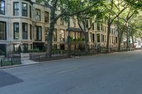 a city sidewalk lined with apartment buildings next to each other, in a row with trees