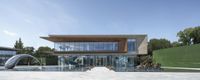 a modern building with a curved glass entrance and walkway going to it and people walking near the pool and fountains