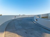 a curved walkway in the middle of an outdoor area near trees and lights on a white wall