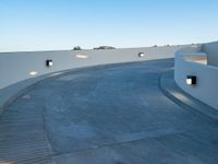 a curved walkway in the middle of an outdoor area near trees and lights on a white wall