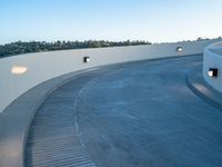 a curved walkway in the middle of an outdoor area near trees and lights on a white wall