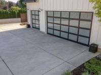 the garage has glass door panels on each side of it while plants adorn the concrete