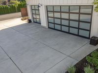 the garage has glass door panels on each side of it while plants adorn the concrete