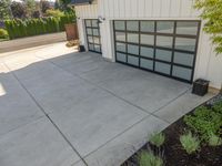 the garage has glass door panels on each side of it while plants adorn the concrete