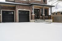 a large brown brick home in the snow with trees in front of it and the driveway covered with snow