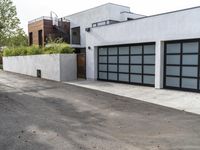 a white garage and brick wall next to an alley way with trees and shrubs surrounding the garage