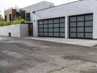 a white garage and brick wall next to an alley way with trees and shrubs surrounding the garage