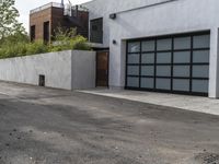 a white garage and brick wall next to an alley way with trees and shrubs surrounding the garage