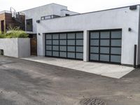 a white garage and brick wall next to an alley way with trees and shrubs surrounding the garage