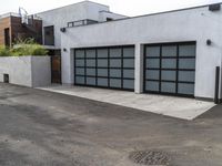 a white garage and brick wall next to an alley way with trees and shrubs surrounding the garage