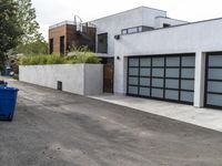 a white garage and brick wall next to an alley way with trees and shrubs surrounding the garage