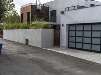 a white garage and brick wall next to an alley way with trees and shrubs surrounding the garage