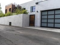 a white garage and brick wall next to an alley way with trees and shrubs surrounding the garage