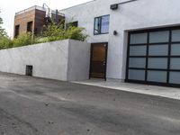 a white garage and brick wall next to an alley way with trees and shrubs surrounding the garage