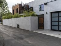 a white garage and brick wall next to an alley way with trees and shrubs surrounding the garage