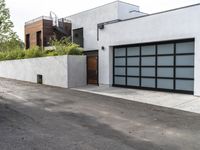 a white garage and brick wall next to an alley way with trees and shrubs surrounding the garage