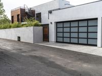 a white garage and brick wall next to an alley way with trees and shrubs surrounding the garage