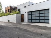 a white garage and brick wall next to an alley way with trees and shrubs surrounding the garage