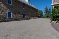 an asphalted driveway is lined with trees and stone houses as a sign for residents to keep up