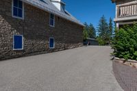 an asphalted driveway is lined with trees and stone houses as a sign for residents to keep up