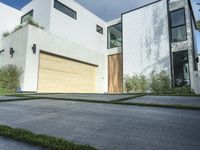 an asphalted driveway with grass in front and a wooden garage on the other side