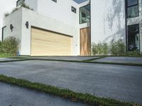 an asphalted driveway with grass in front and a wooden garage on the other side