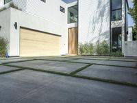 an asphalted driveway with grass in front and a wooden garage on the other side