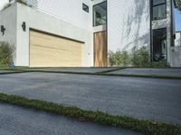 an asphalted driveway with grass in front and a wooden garage on the other side