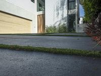 an asphalted driveway with grass in front and a wooden garage on the other side