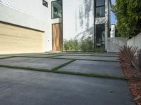 an asphalted driveway with grass in front and a wooden garage on the other side