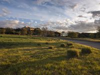 a grassy field that contains some bales and a road in the background as sun rises