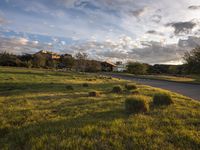 a grassy field that contains some bales and a road in the background as sun rises