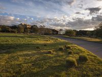 a grassy field that contains some bales and a road in the background as sun rises