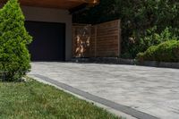 a driveway is shown with a garage door in the distance behind it and landscaping around it