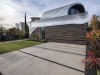 a house with a wooden exterior has a sloping metal facade and is on a grassy area