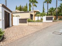 a house that has palm trees outside of it and a driveway to the garage area