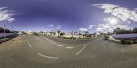 a panoramic lens shot of an intersection with some white fences and buildings in the background