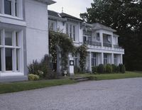 a view of a large house near a street and some trees in the background with flowers