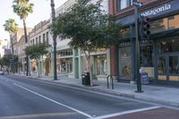 an empty street with a lot of stores and palm trees in front of it and two cars passing by the curb