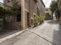 an empty cobblestone road with a stone building and lots of trees and bushes