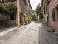 an empty cobblestone road with a stone building and lots of trees and bushes