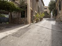 an empty cobblestone road with a stone building and lots of trees and bushes