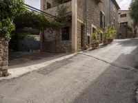 an empty cobblestone road with a stone building and lots of trees and bushes