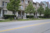 an empty street and some buildings on both sides of the road, with the green grass between the two trees